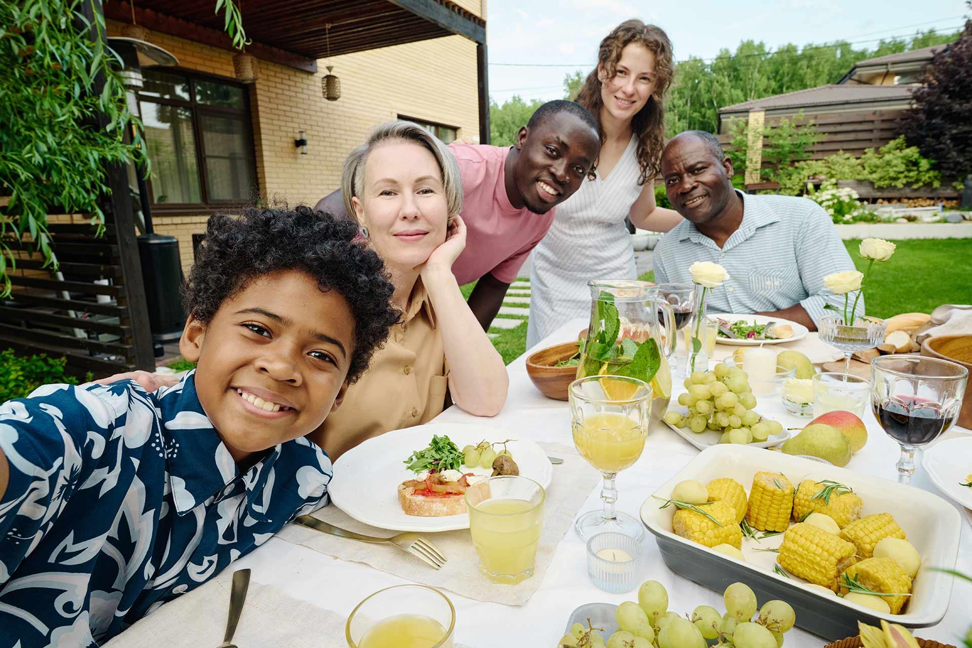 Cute African American Boy in Hawaiian Shirt Taking Selfie With His Parents and Grandparents While Sitting by Served Table During Family Dinner